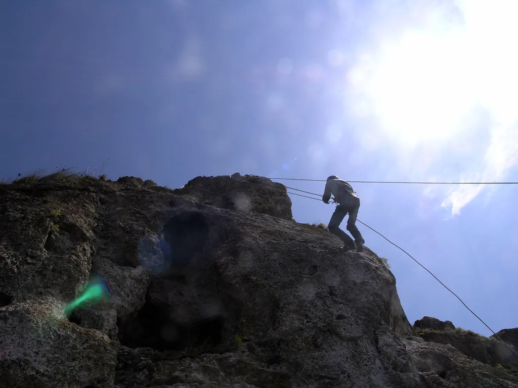 Alpinist coborând în rapel de pe un perete de calcar din toltre